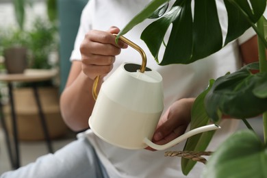 Photo of Houseplant care. Woman watering beautiful monstera with water indoors, closeup