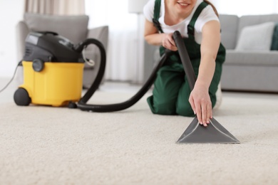 Photo of Female worker cleaning carpet with vacuum in living room