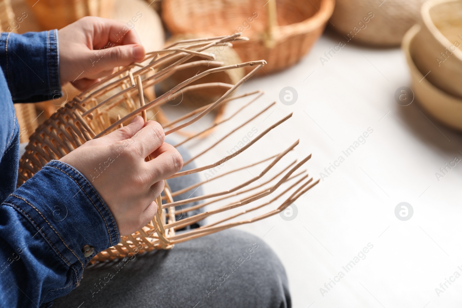 Photo of Woman weaving wicker basket indoors, closeup view