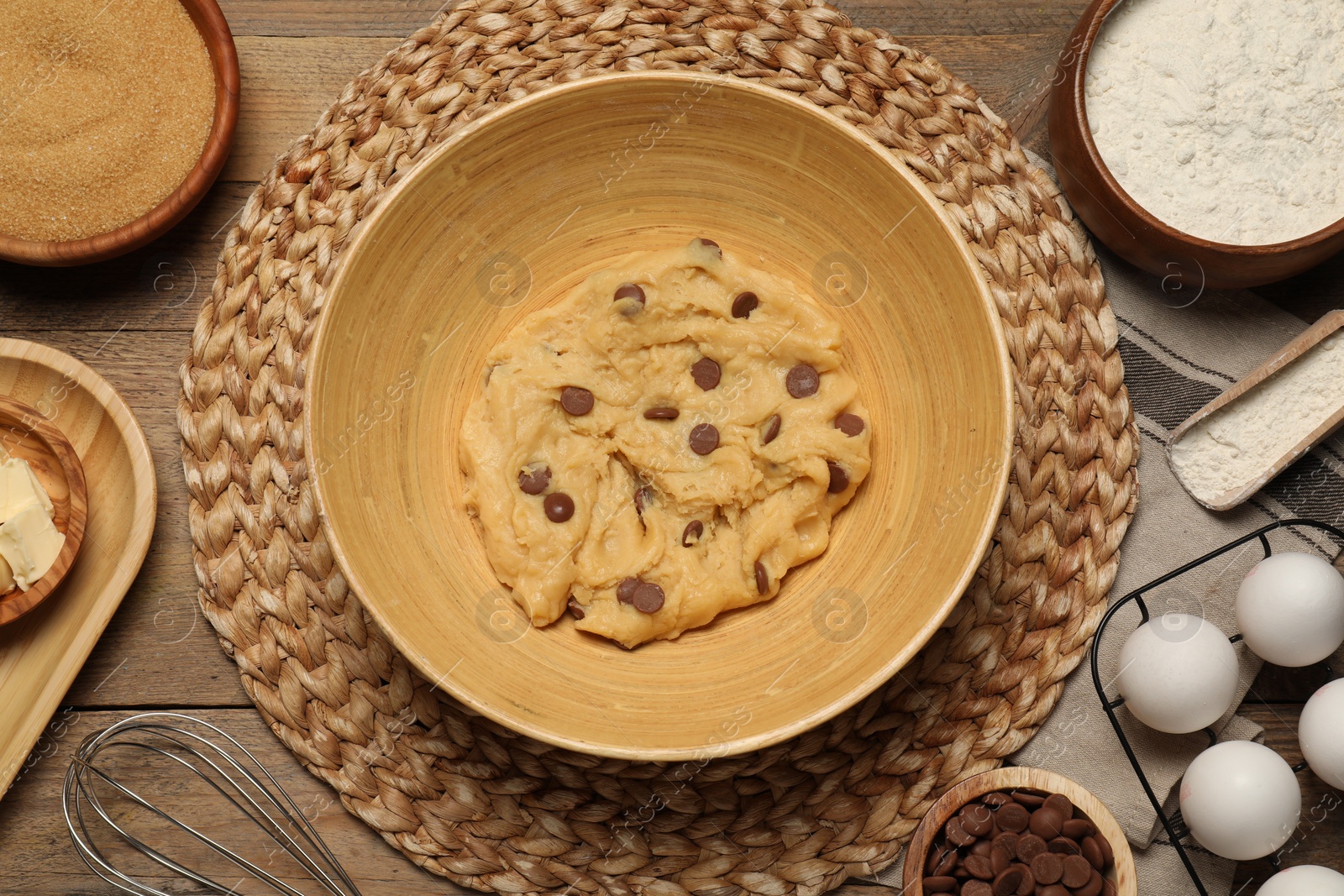 Photo of Fresh dough and different ingredients for cooking chocolate chip cookies on wooden table, flat lay