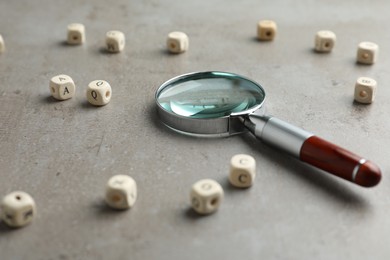 Photo of Magnifier glass and cubes with letters on light grey stone background, closeup. Find keywords concept