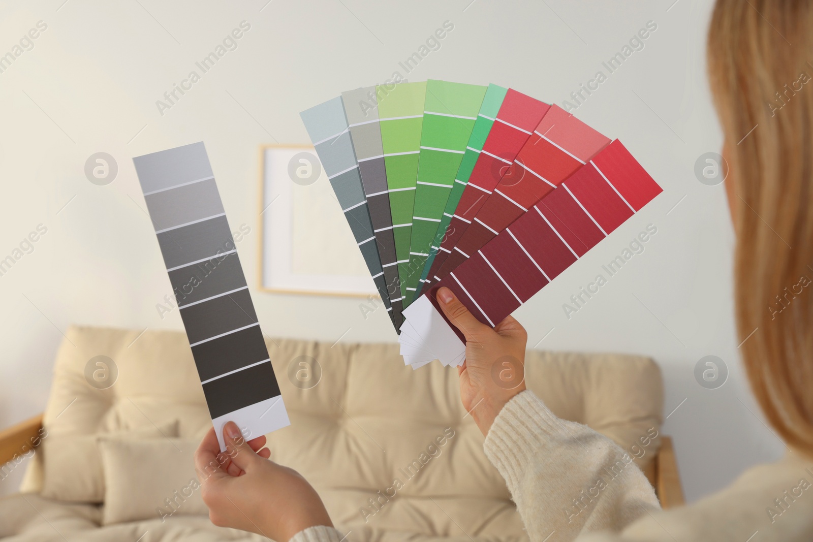 Photo of Woman choosing color for wall in room, focus on hands with paint chips. Interior design