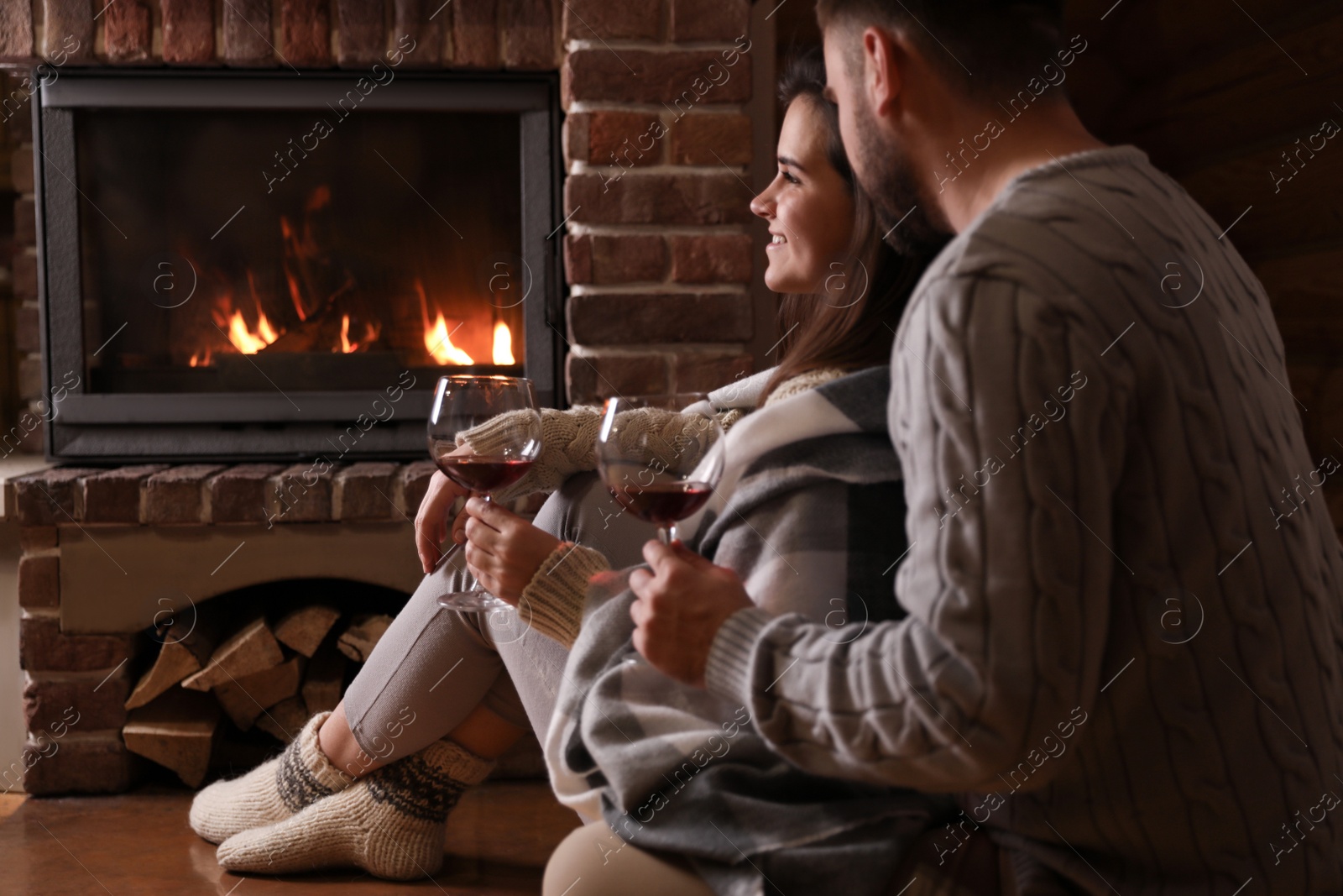 Photo of Lovely couple with glasses of wine near fireplace at home. Winter vacation