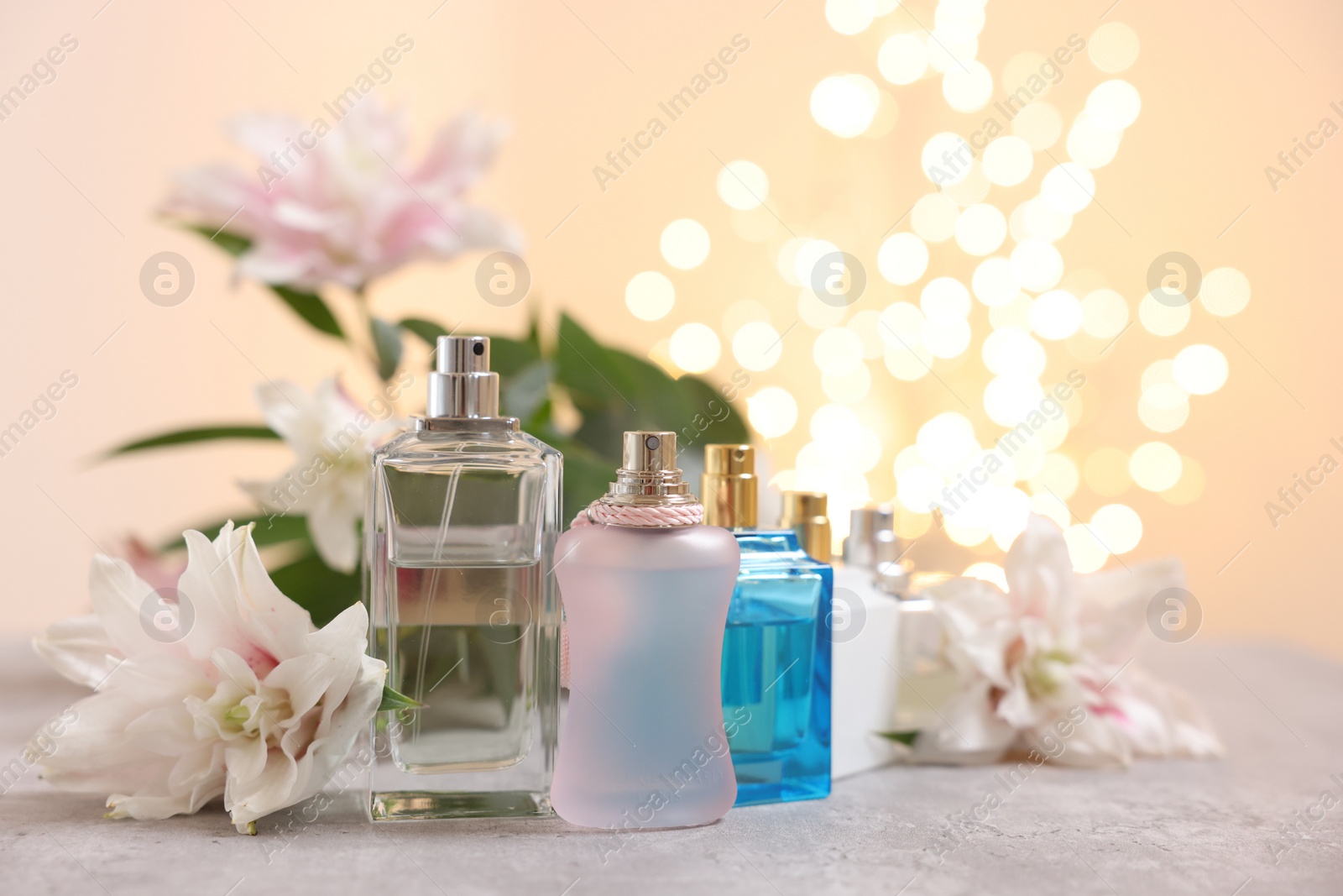 Photo of Perfume bottles and bouquet of beautiful lily flowers on table against beige background with blurred lights, closeup