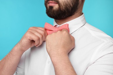 Photo of Man in shirt adjusting bow tie on light blue background, closeup