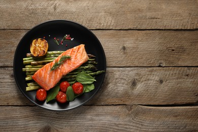 Tasty grilled salmon with tomatoes, asparagus and spices on wooden table, top view. Space for text