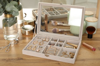 Photo of Elegant jewelry box with beautiful bijouterie, cosmetics and candles on wooden table