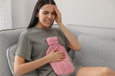 Photo of Woman using hot water bottle to relieve abdominal pain at home