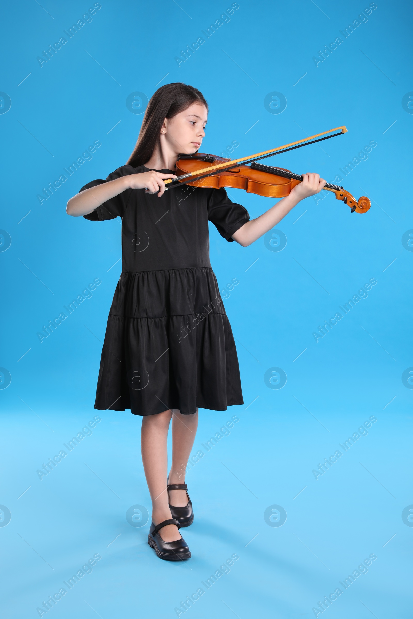 Photo of Preteen girl playing violin on light blue background