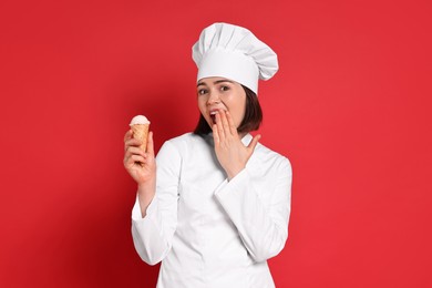 Photo of Happy confectioner with delicious ice cream cone on red background