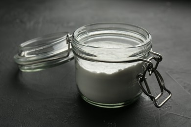 Photo of Baking powder in jar on black textured table, closeup