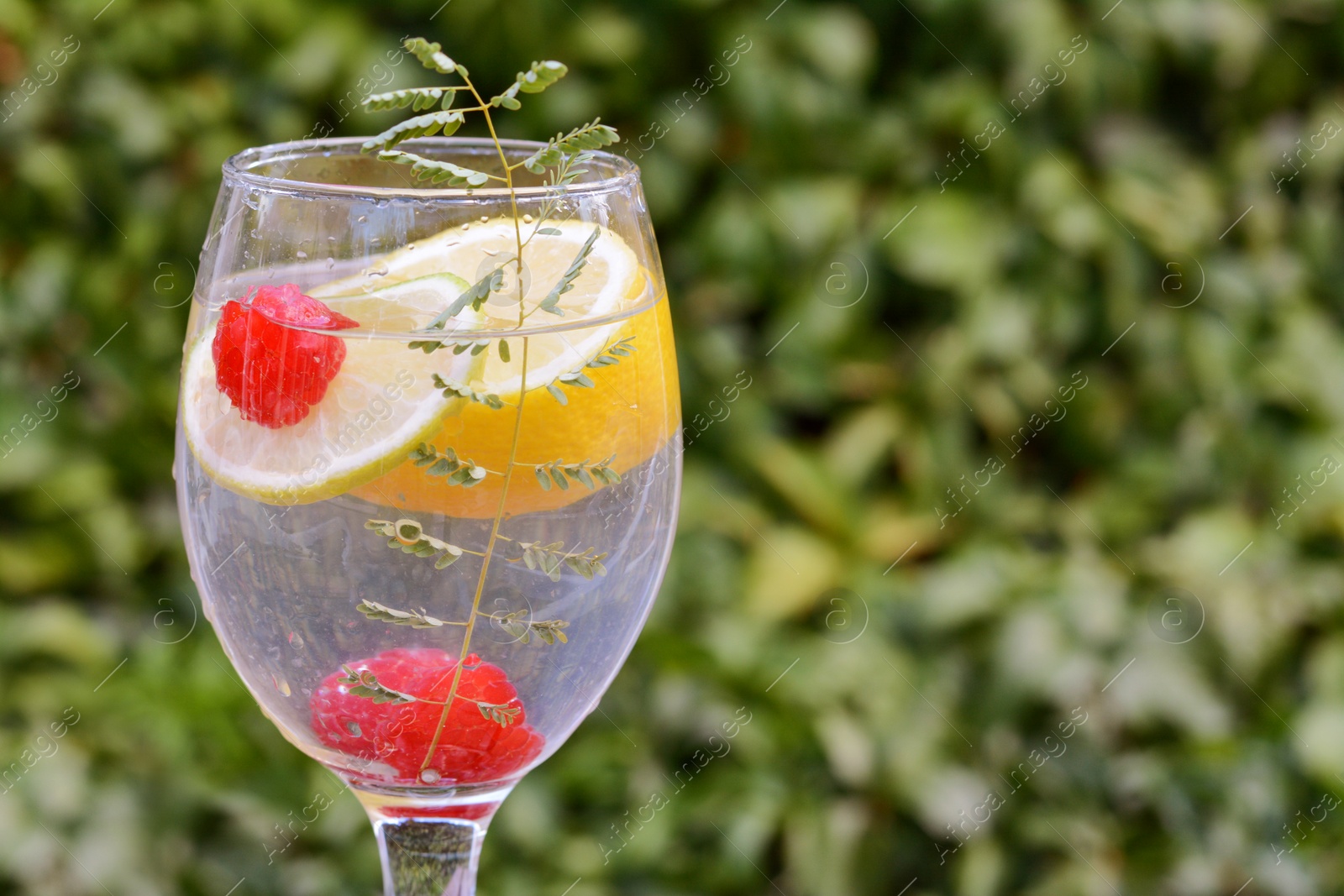 Photo of Delicious refreshing lemonade with raspberries against green blurred background, closeup. Space for text