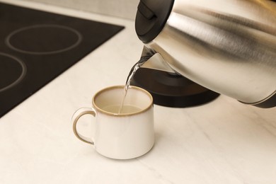 Pouring hot water from electric kettle into cup in kitchen, closeup