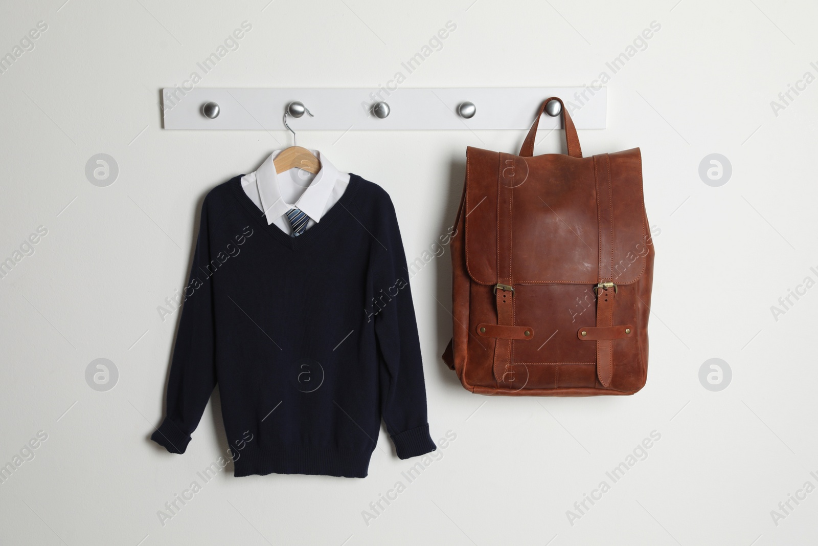 Photo of Shirt, jumper and bag hanging on white wall. School uniform