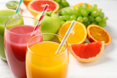 Glasses of different juices with straws and fresh fruits on wooden background, closeup