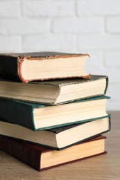 Photo of Stack of old hardcover books on wooden table near white brick wall