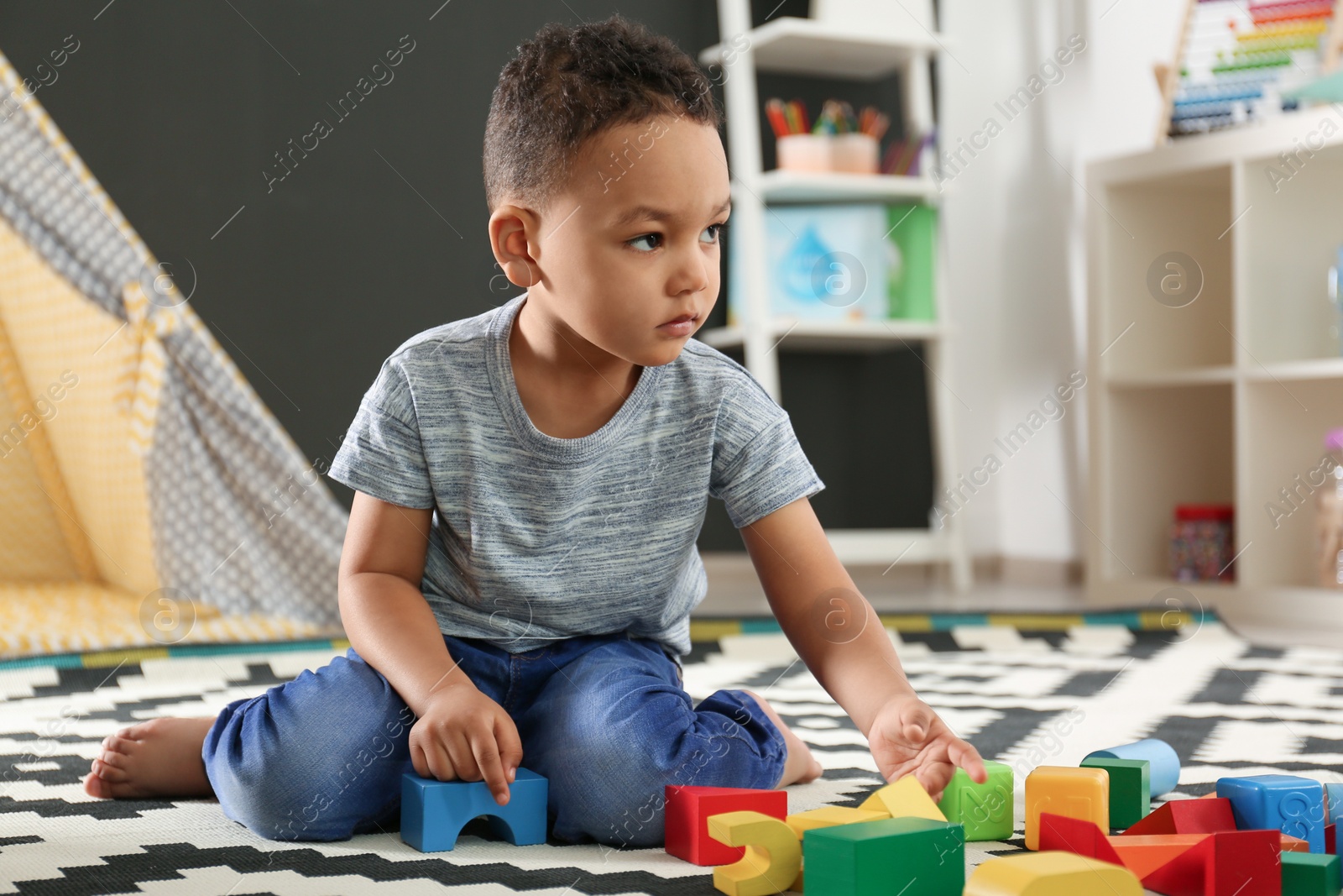 Photo of Cute little African-American child playing with building blocks on floor in kindergarten. Indoor activity