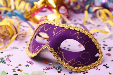 Photo of Beautiful carnival mask and party decor on violet background, closeup
