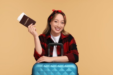 Happy young woman with passport, ticket and suitcase on beige background