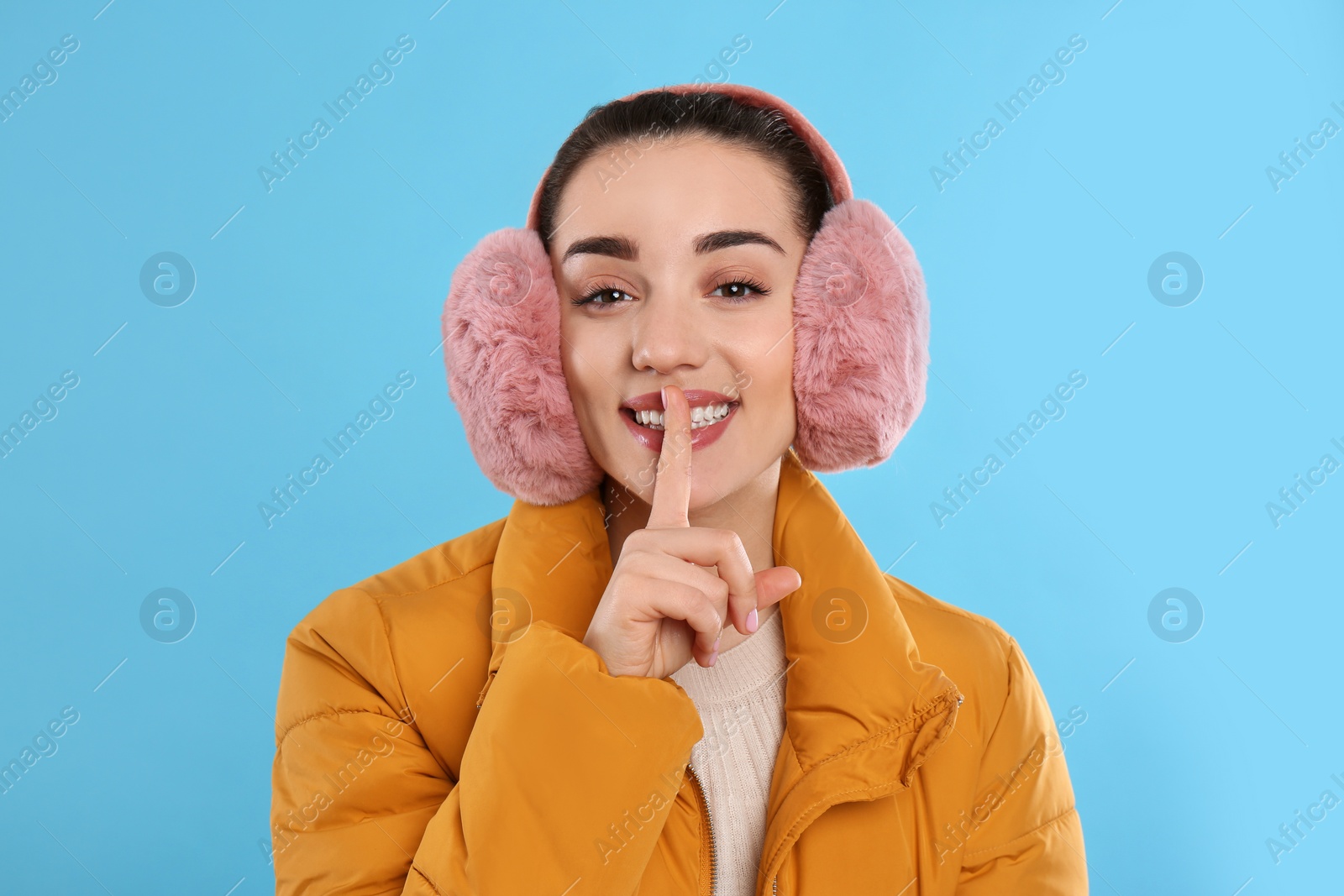 Photo of Beautiful young woman wearing earmuffs on light blue background