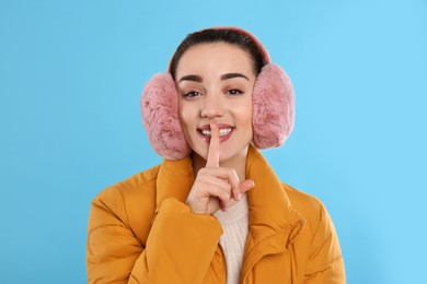 Beautiful young woman wearing earmuffs on light blue background