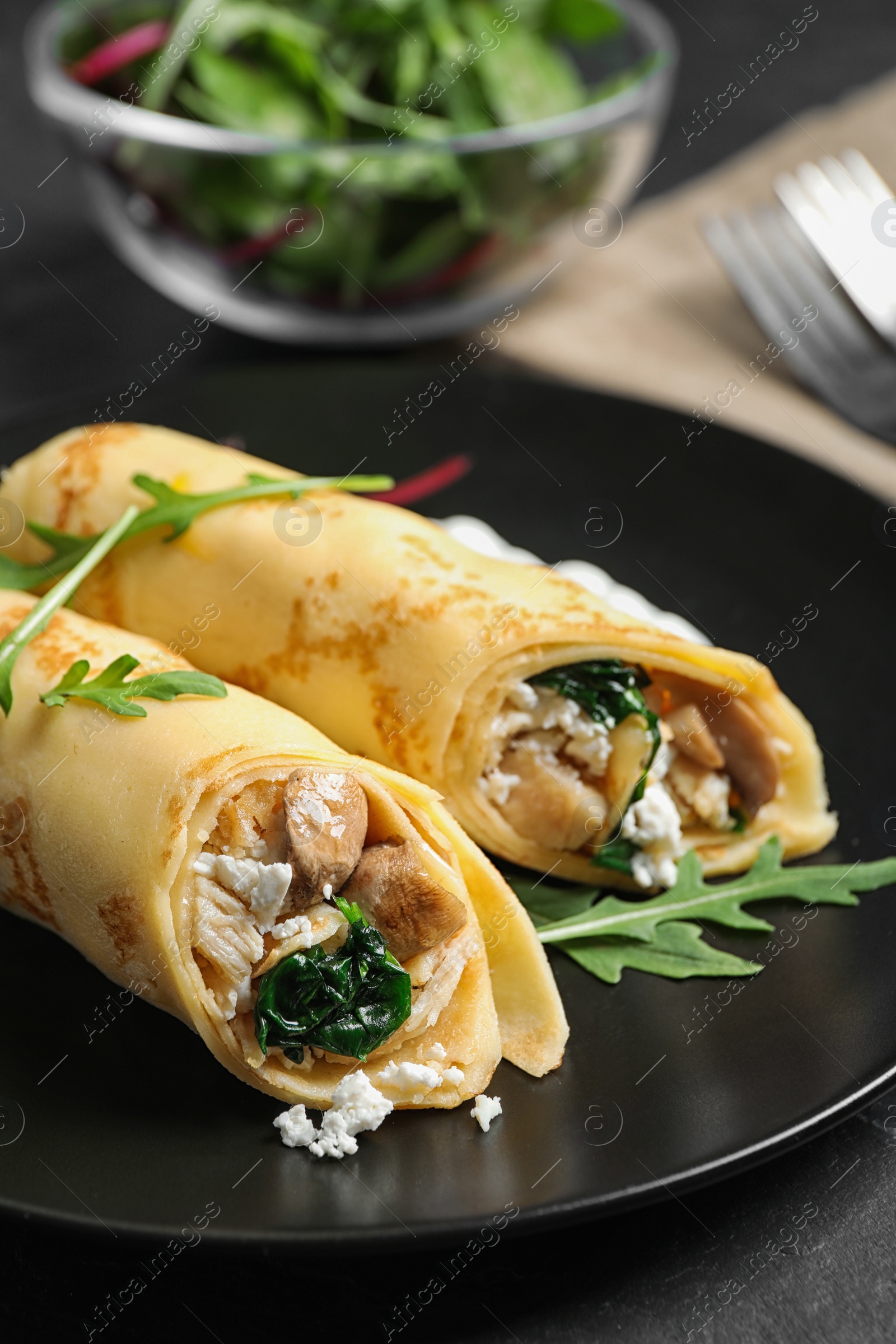 Photo of Delicious thin pancakes with chicken and mushrooms on black table, closeup