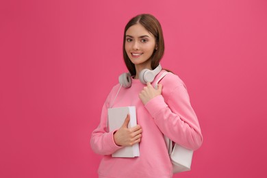 Photo of Teenage student with book, headphones and backpack on pink background