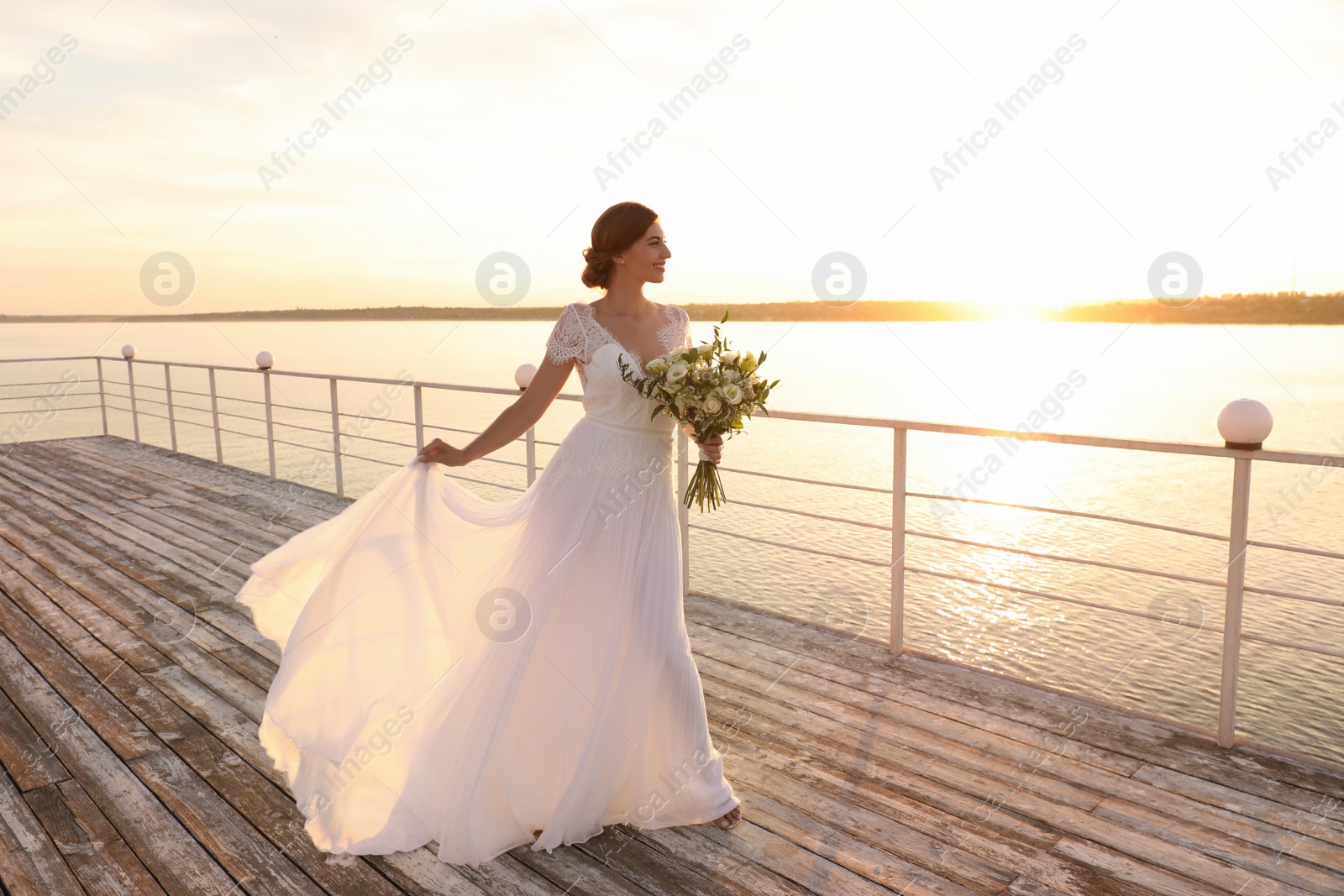 Photo of Gorgeous bride in beautiful wedding dress with bouquet near river on sunset