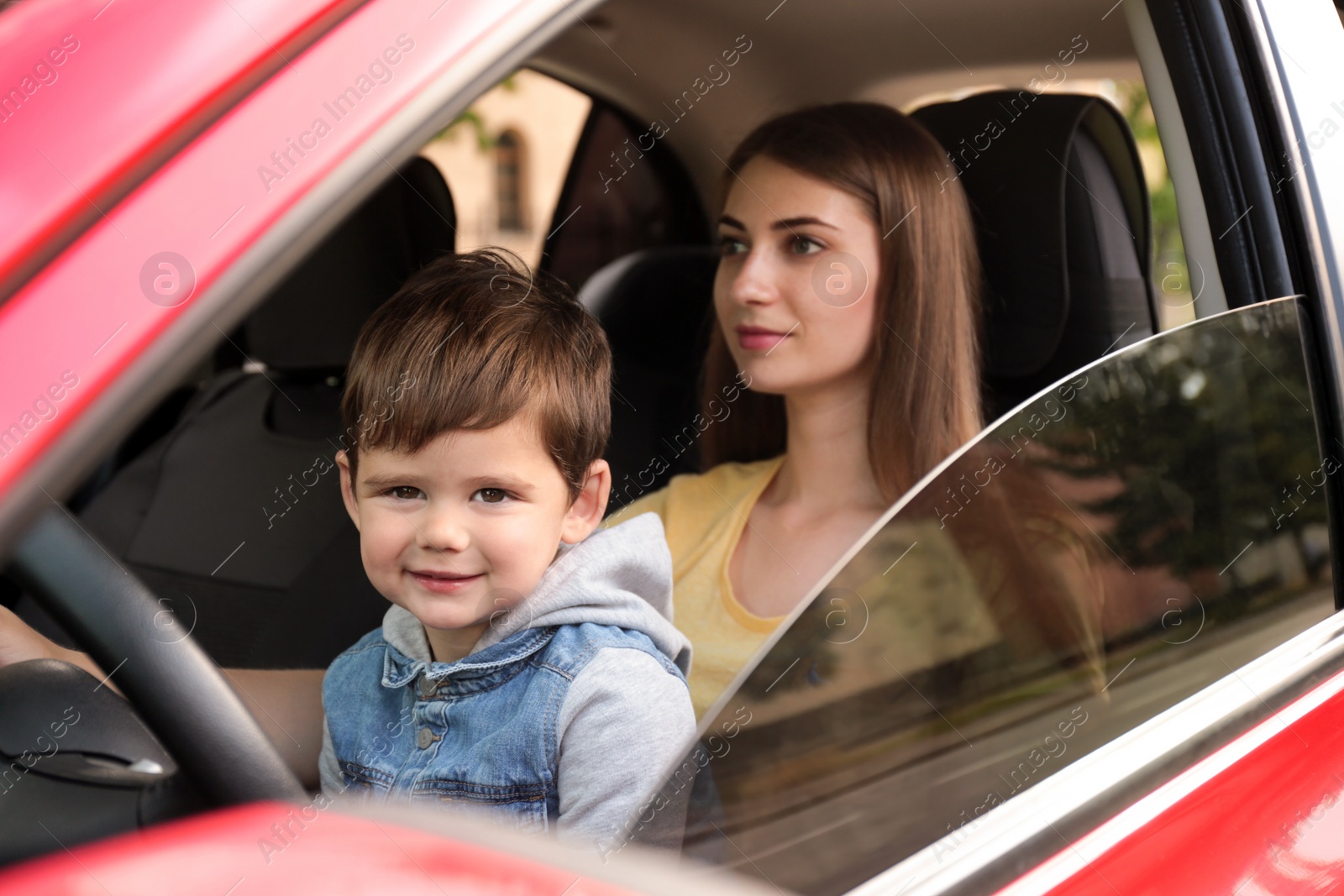 Photo of Mother with little son driving car together. Child in danger