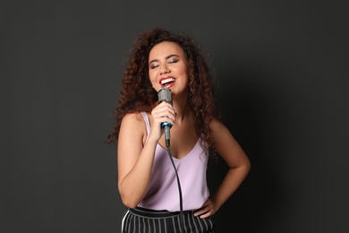 Curly African-American woman in stylish clothes singing with microphone on black background