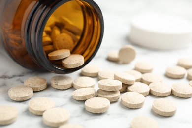 Bottle with vitamin pills on white marble table, closeup