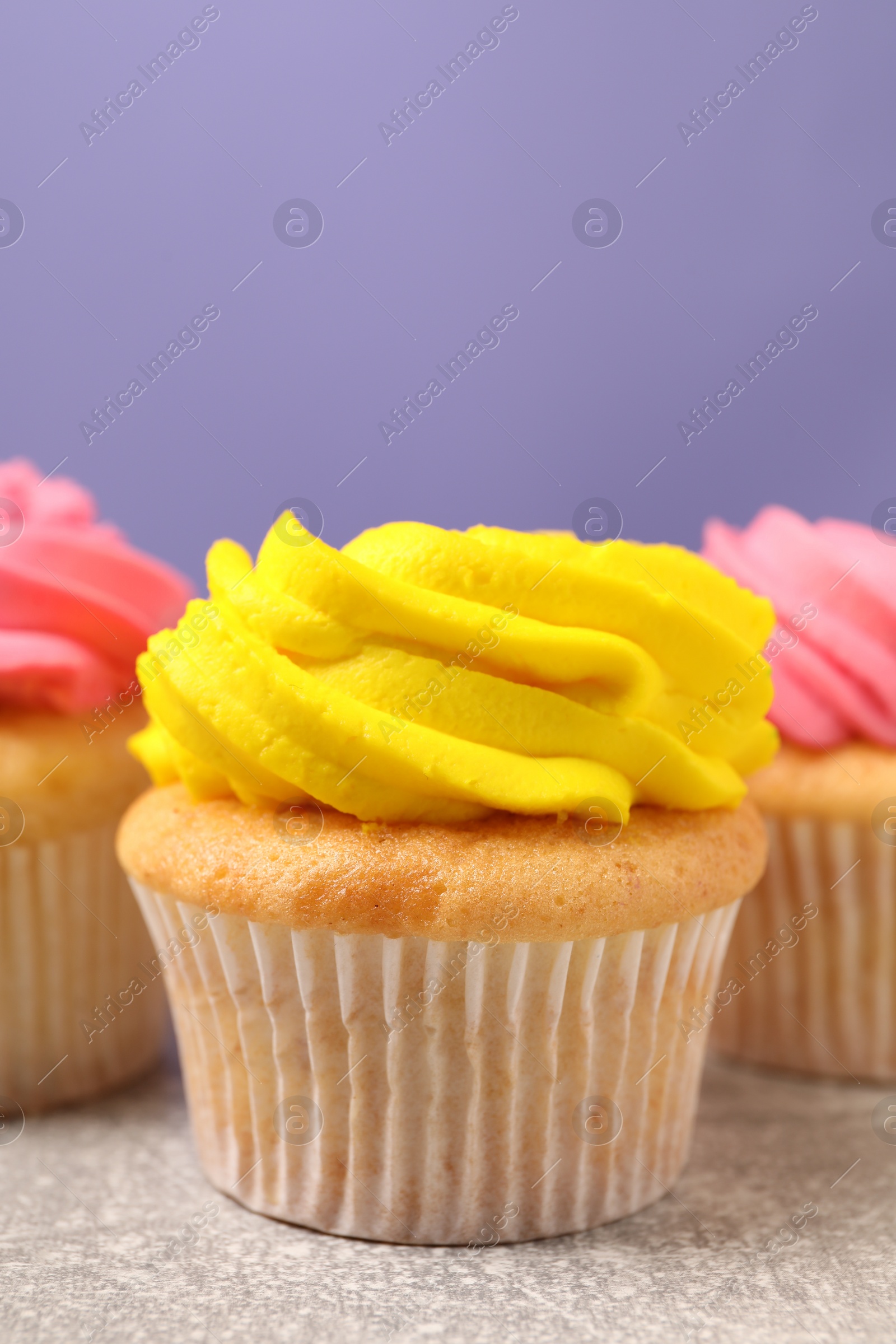 Photo of Delicious cupcakes with bright cream on gray table against violet background, space for text