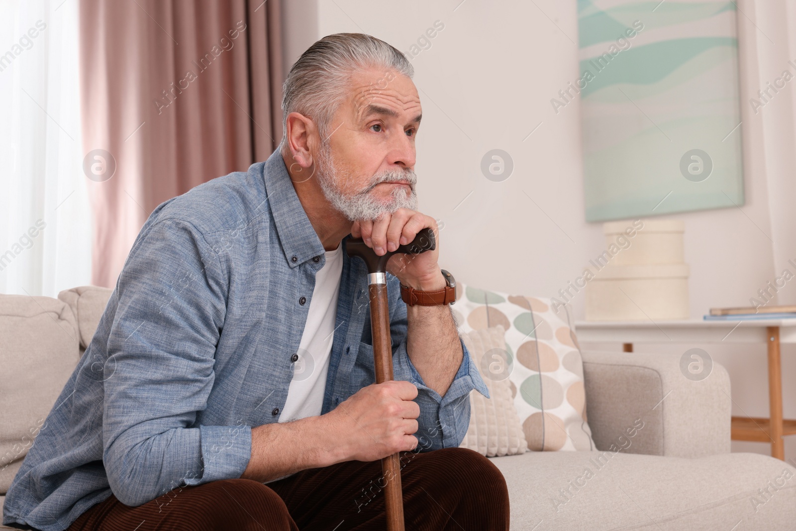 Photo of Senior man with walking cane sitting on sofa at home. Space for text