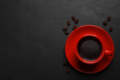 Photo of Red cup with aromatic coffee and beans on black textured table, flat lay. Space for text