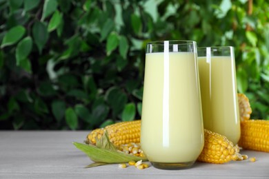 Photo of Tasty fresh corn milk and cobs on light table against blurred background. Space for text