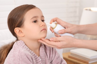 Photo of Mother using nasal spray to treat her little daughter indoors, closeup