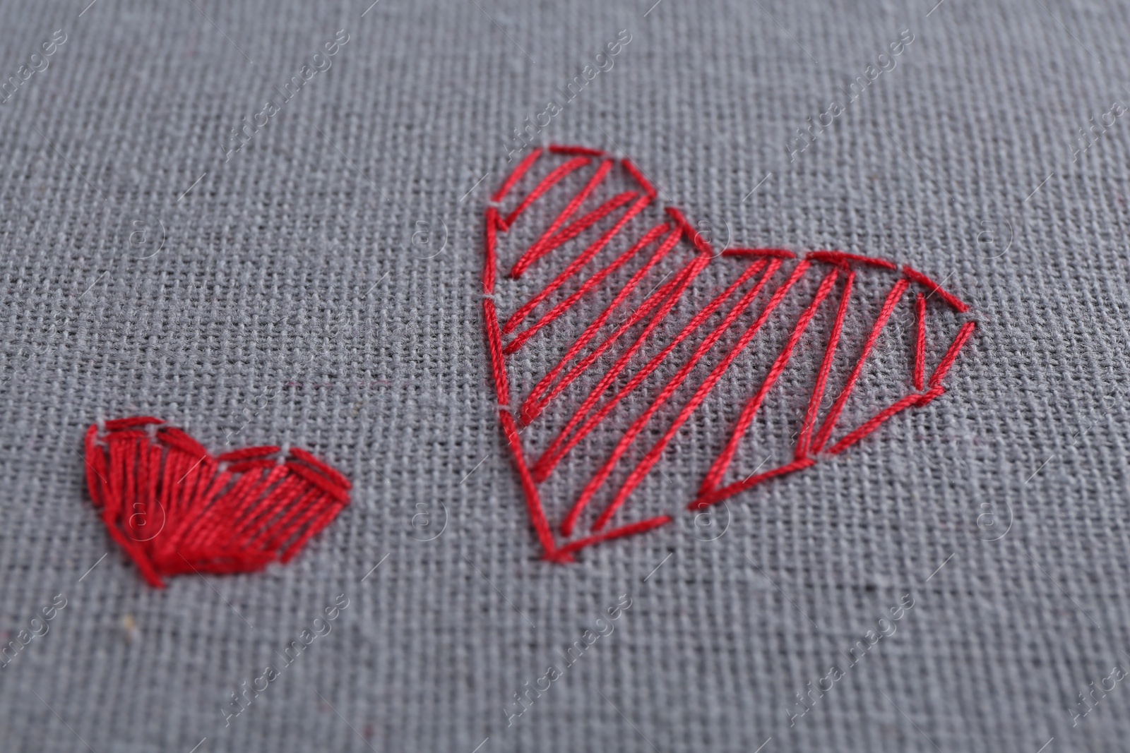 Photo of Embroidered red hearts on light grey cloth, closeup