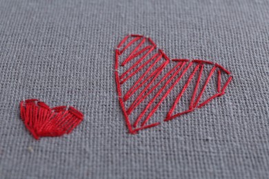 Photo of Embroidered red hearts on light grey cloth, closeup