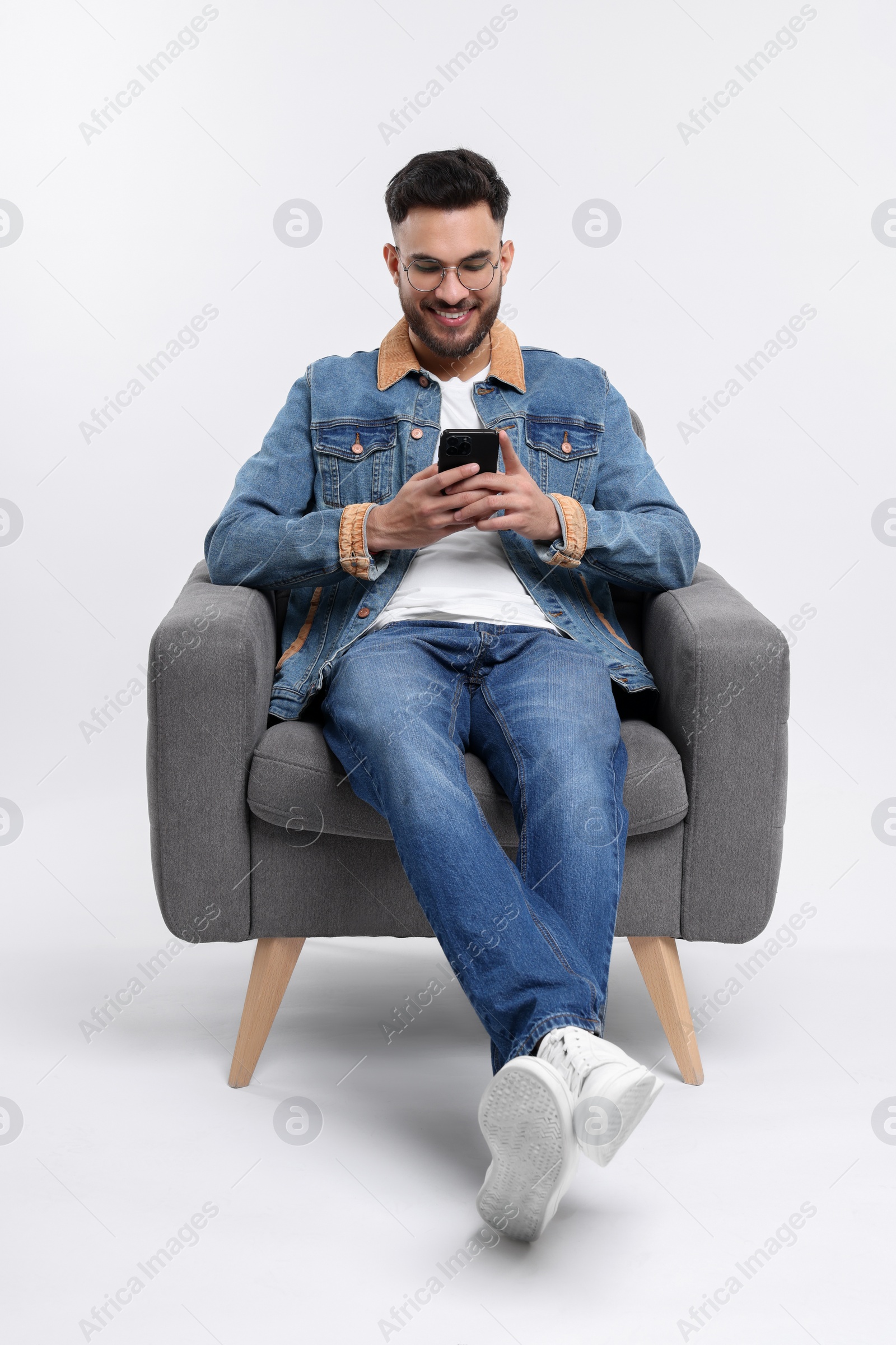 Photo of Happy man using smartphone in armchair on white background