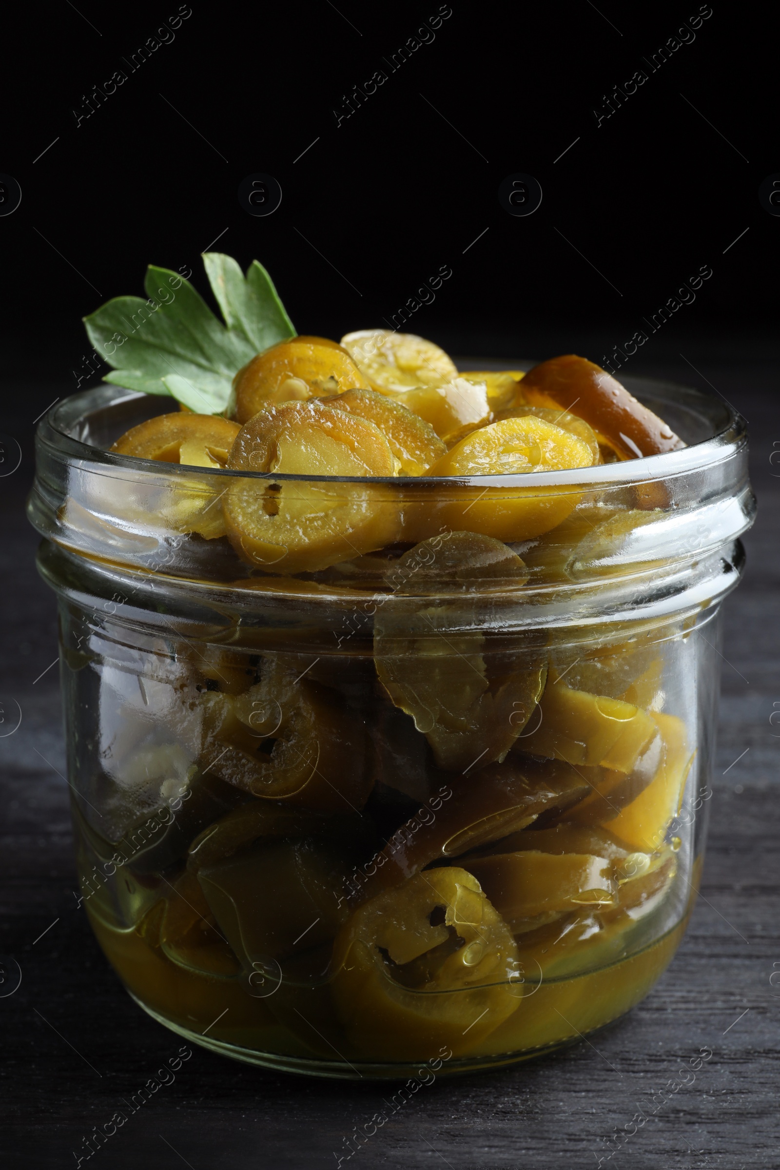 Photo of Glass jar with slices of pickled green jalapeno peppers on black wooden table