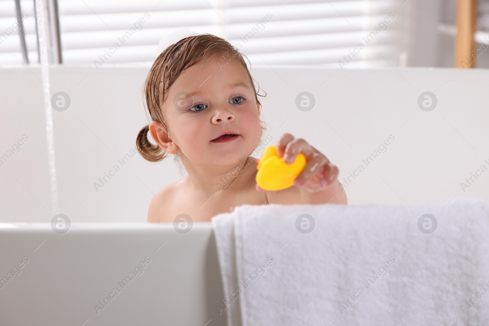 Photo of Cute little girl taking bath with toy indoors