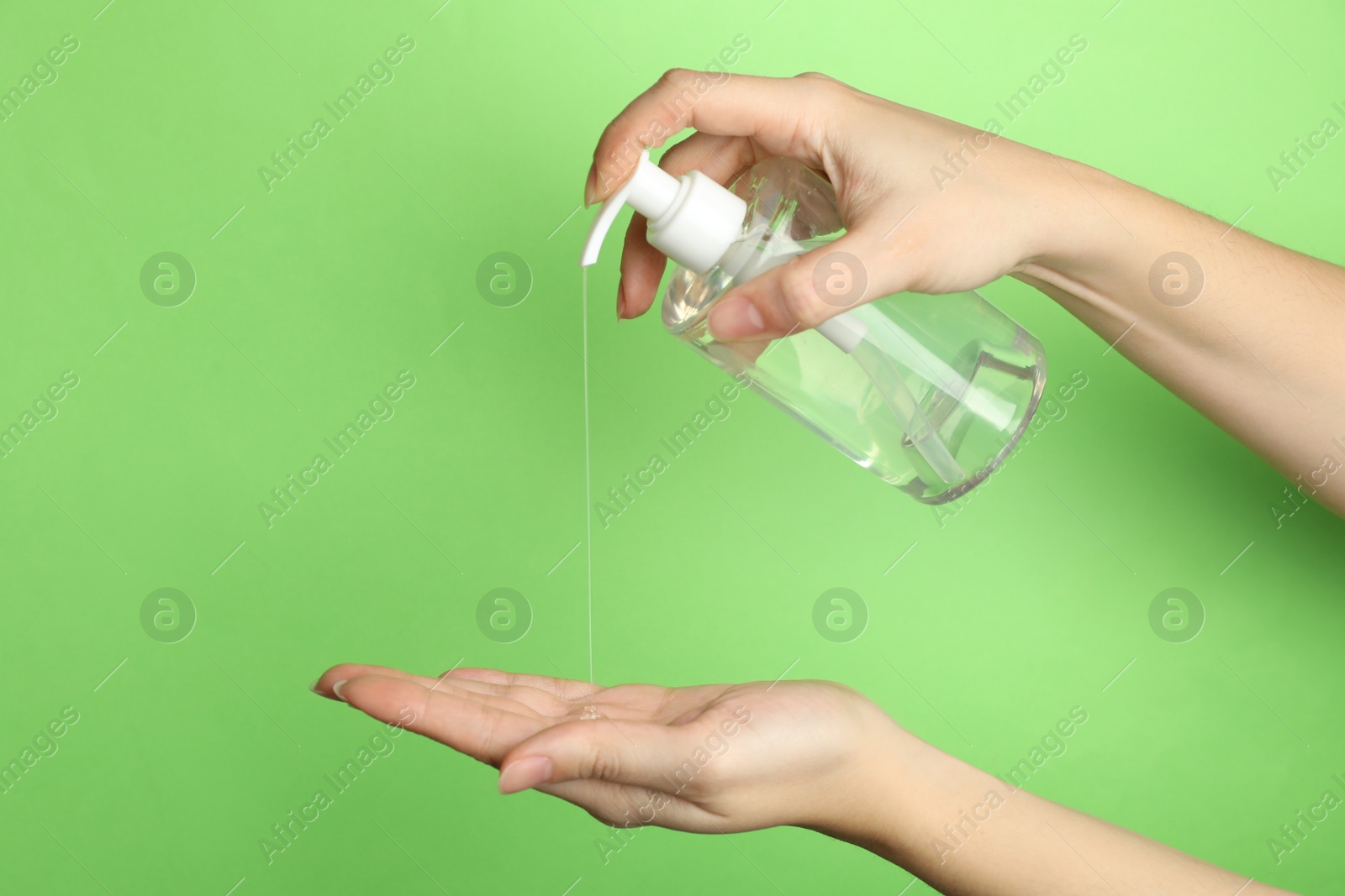 Photo of Woman applying antiseptic gel on hand against green background, closeup
