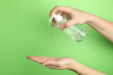 Woman applying antiseptic gel on hand against green background, closeup