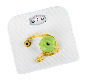 Photo of Weight loss concept. Ripe apple and measuring tape on scales isolated on white, top view