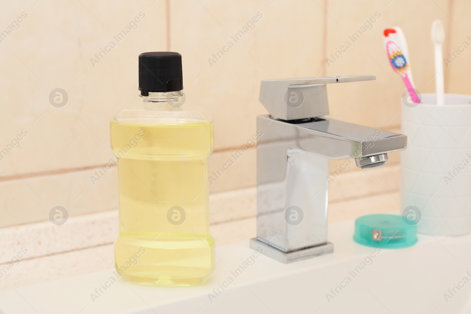 Photo of Mouthwash and holder with toothbrushes on sink in bathroom. Teeth and oral care