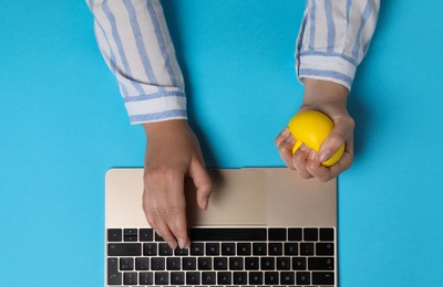 Photo of Woman squeezing antistress ball while working with laptop on light blue background, top view