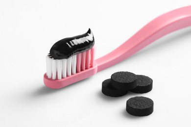 Brush with charcoal toothpaste and pills on white background