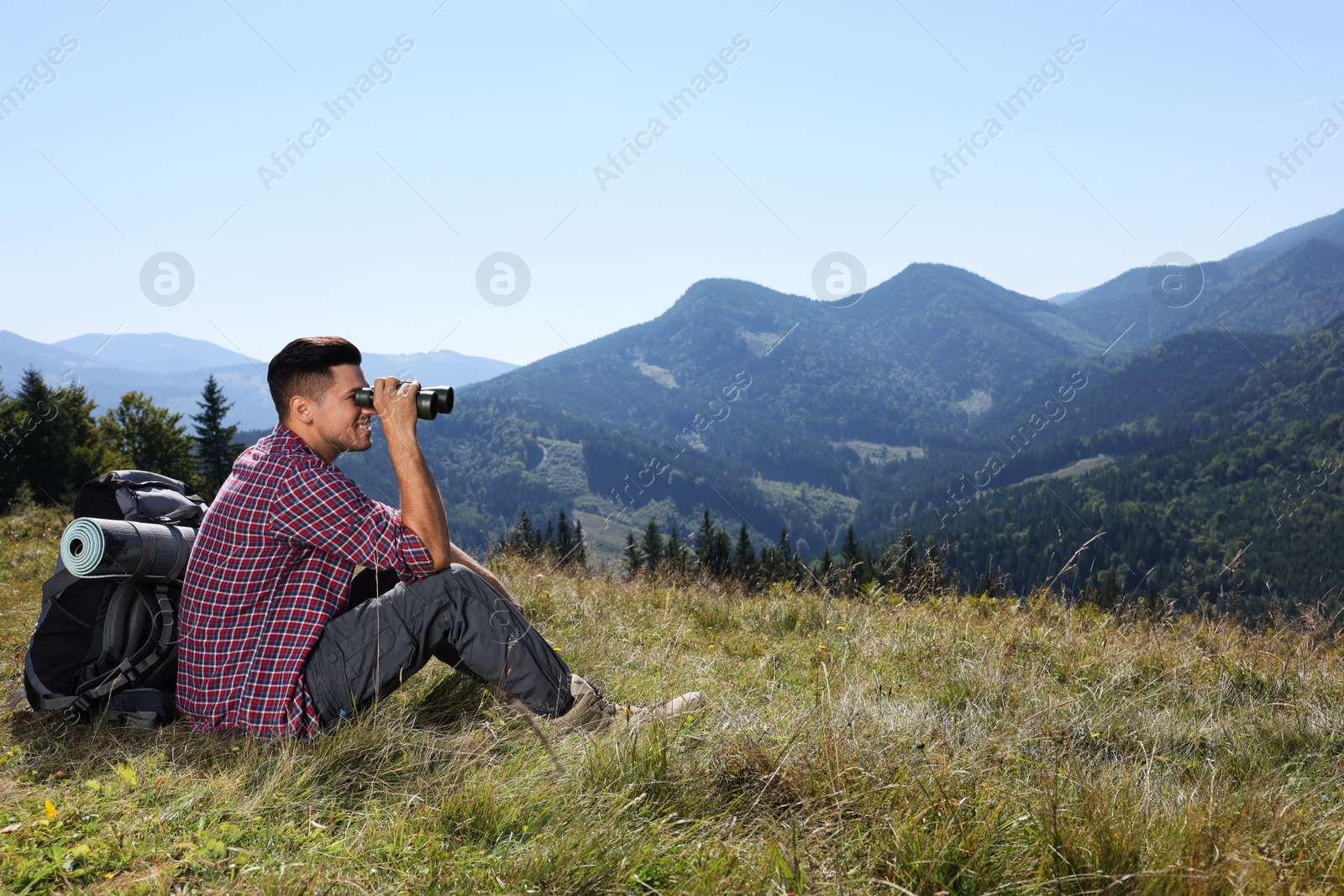 Photo of Tourist with hiking equipment looking through binoculars in mountains