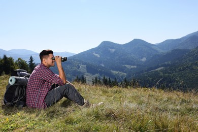 Photo of Tourist with hiking equipment looking through binoculars in mountains