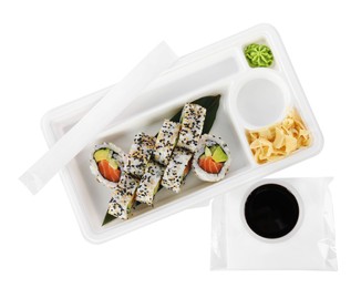 Photo of Food delivery. Plastic container with delicious sushi rolls and bowl of soy sauce on white background, top view